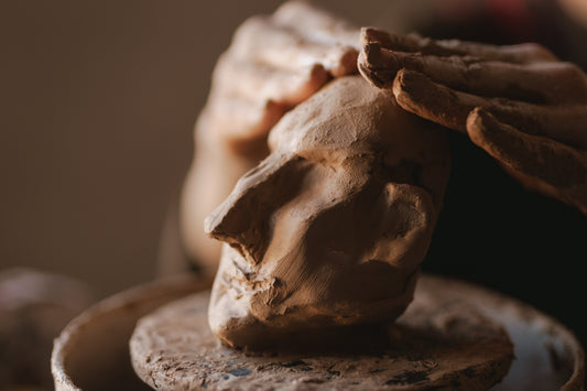 Close-up of hands molding clay into a sculpture, representing the tactile materiality and human craft of the Mitsooz collection.