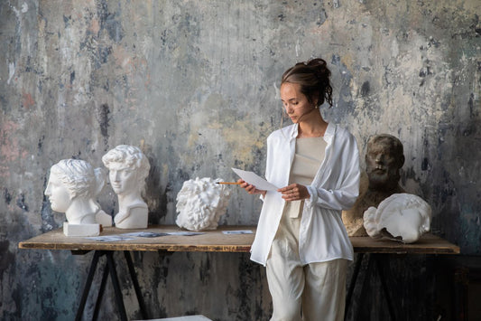  A woman in a minimalist architectural space featuring large-scale sculptures from the Mitsooz collection, illustrating narrative weight and art as a primary design element.