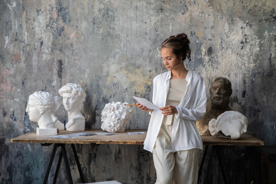 A woman in a minimalist architectural space featuring large-scale sculptures from the Mitsooz collection, illustrating narrative weight and art as a primary design element.