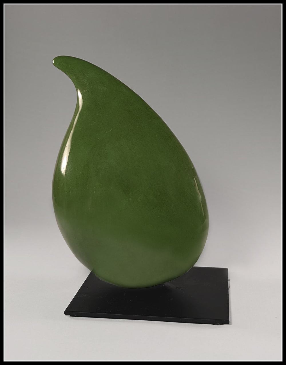 A vertical green porcelain sculpture titled Bean Cinq by Andree Brown featuring a sleek, hand-formed organic seed shape on a black metal base on Mitsooz.