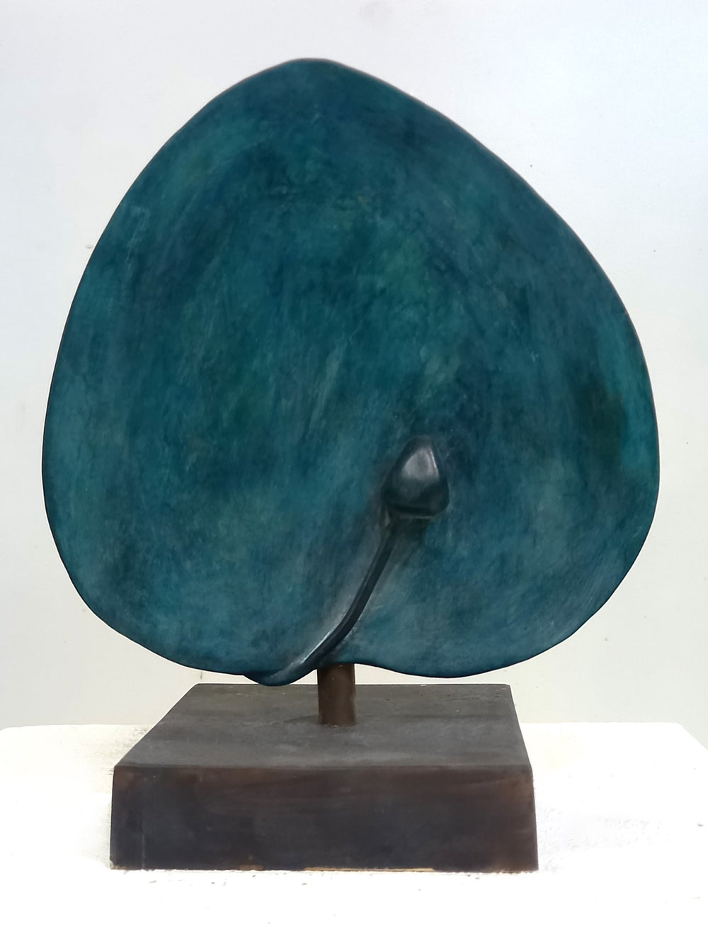 A vertical 10lb bronze sculpture titled Caper Leaf and Blossom by Andrée Brown featuring a hand-formed rounded leaf with a deep teal studio patina on a bronze pedestal base on Mitsooz.