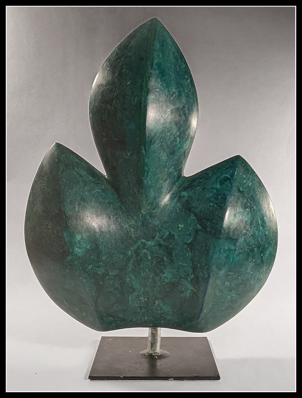 A vertical bespoke bronze sculpture titled Fig Leaf by Andree Brown featuring a hand-formed three-lobed leaf with a polished green verdigris patina on a black metal base on Mitsooz.