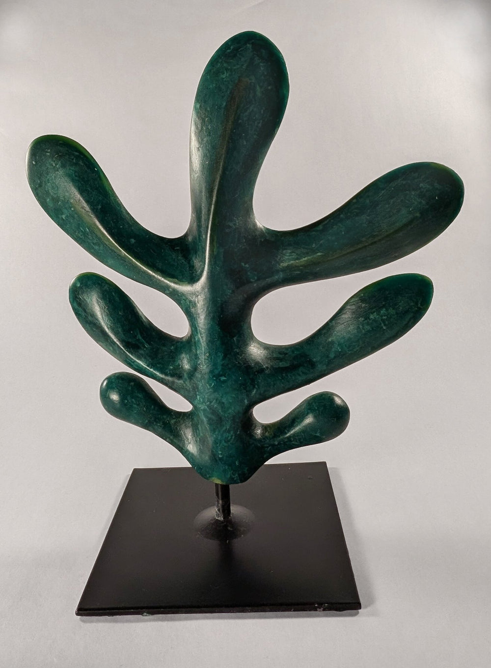 A vertical custom porcelain and metal sculpture titled Pine Oak Leaf by Andree Brown featuring a hand-formed multi-lobed leaf in forest green on a black pedestal base on Mitsooz.