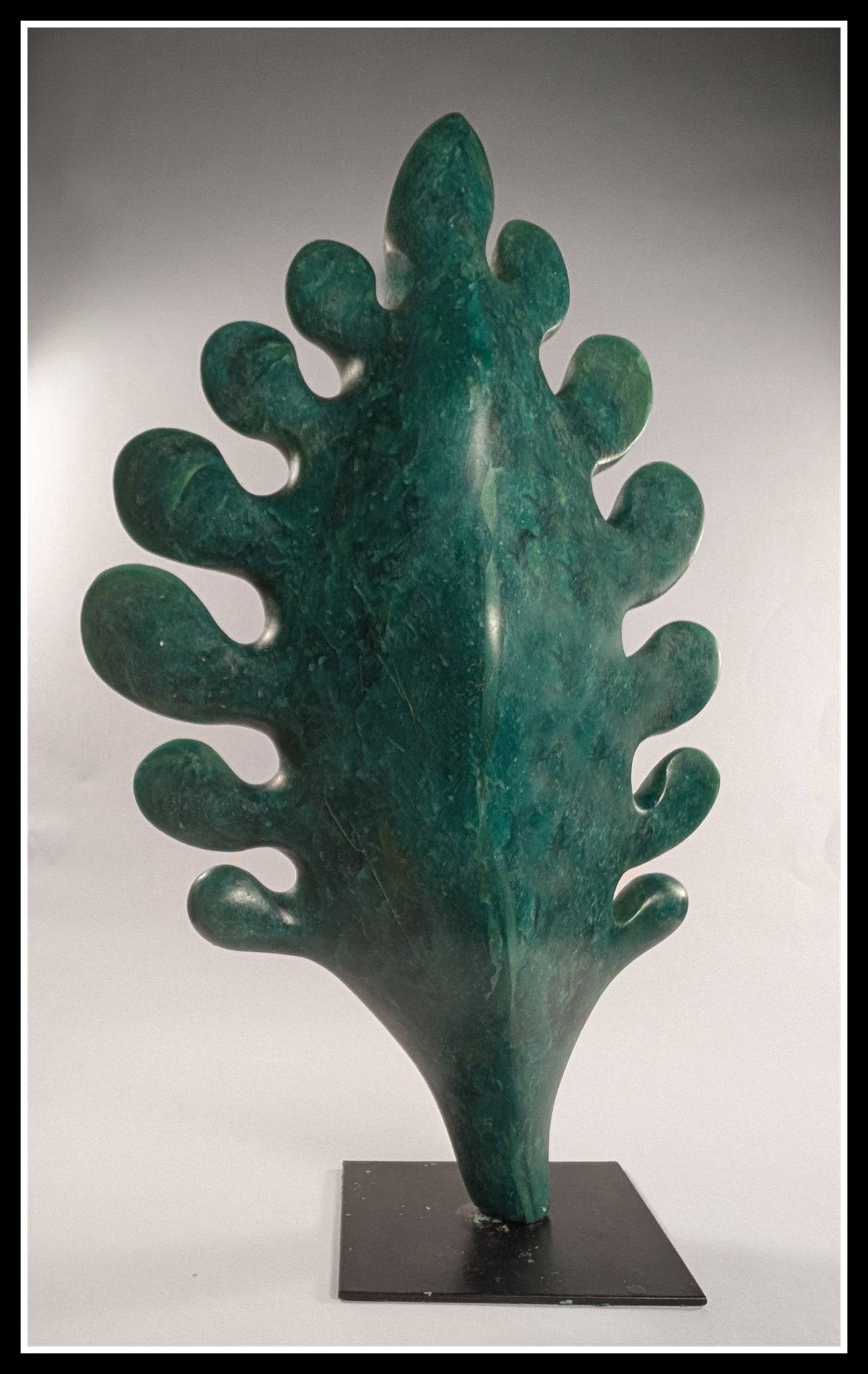 A vertical bespoke bronze sculpture titled White Oak Leaf by Andrée Brown featuring a large hand-formed oak leaf with a rich forest green studio patina on a black metal base on Mitsooz.