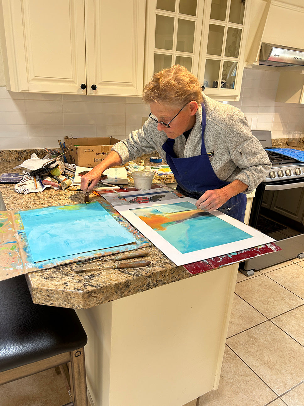 Contemporary abstract artist Kari Bell, a featured maker at Mitsooz, engaged in the intricate process of oil and cold wax painting. The image showcases her tactical layering technique and studio environment, illustrating how she translates the light and colors of the Southwest into bold, textured compositions.