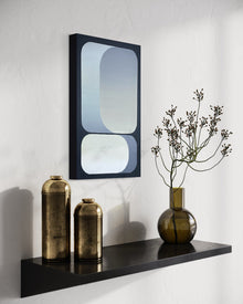 A vertical 15x24 original abstract painting titled Rising by Kevin Cross, featuring luminous blue and slate grey geometric gradients. The artwork is styled in a high-end interior on a black floating shelf alongside weathered gold canisters and a brown glass vase with budding branches on Mitsooz.