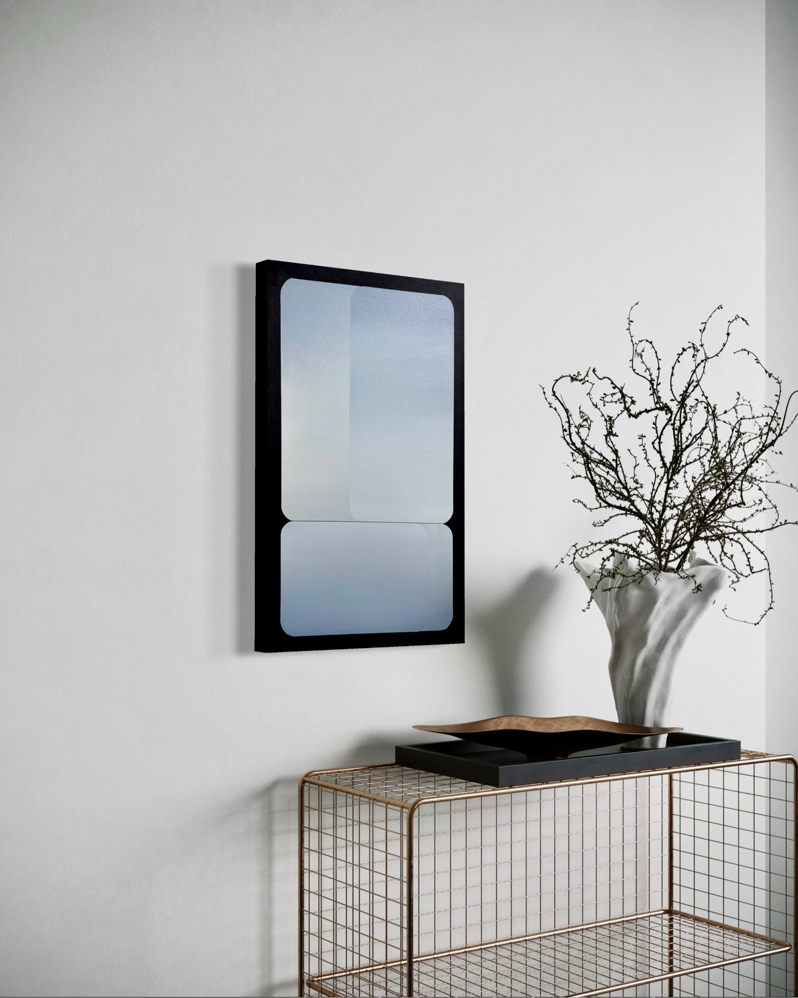 A 15x24 vertical original abstract painting titled Stacked by Kevin Cross, featuring overlapping silver and cool blue gradients in rounded geometric fields with a black border. The artwork is styled in a sophisticated modern interior above a gold wire console table featuring a tall, textured white vase with delicate branches on Mitsooz.