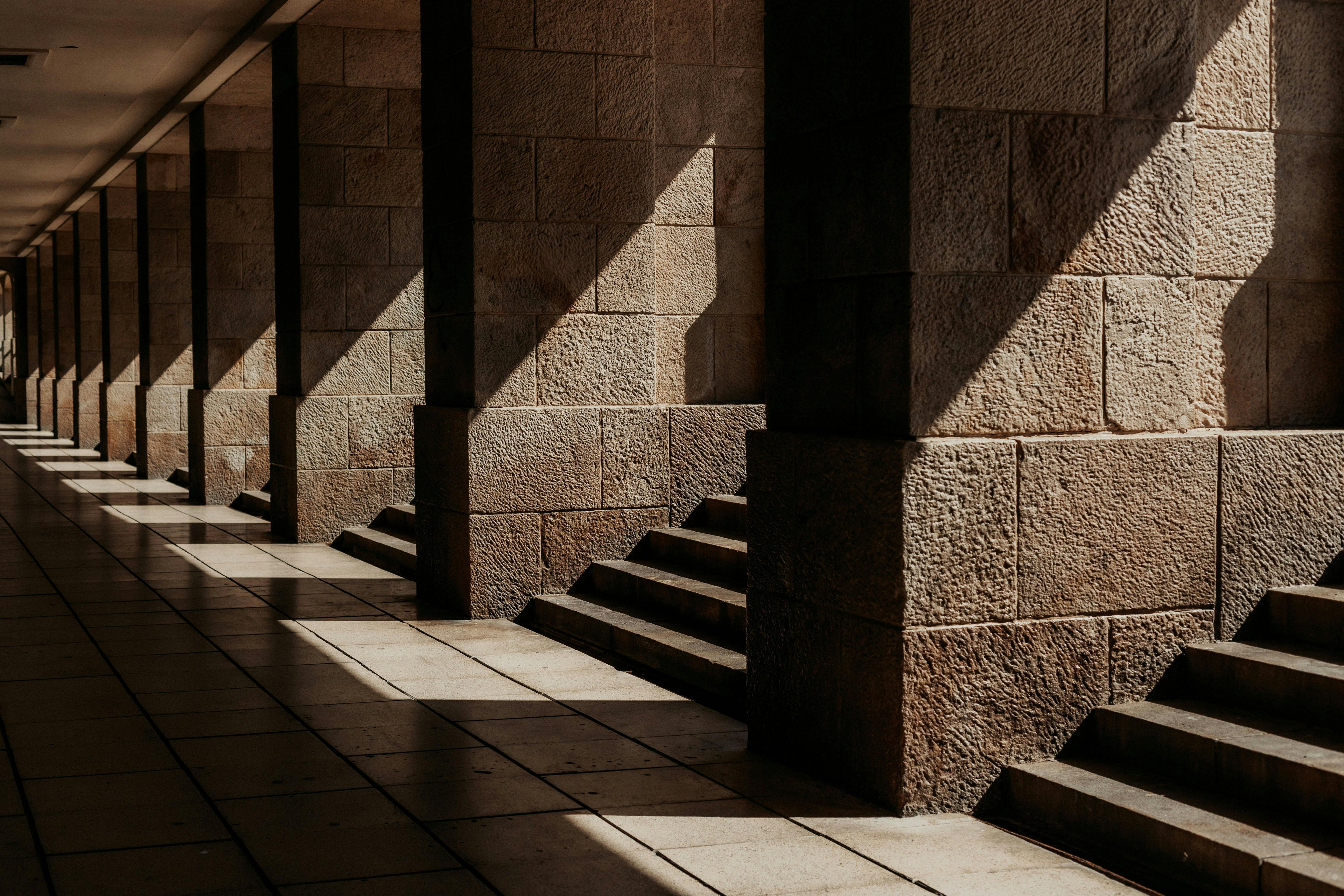 Architectural stone columns and dramatic shadows representing the authoritative Press Room and media headquarters. Mitsooz.