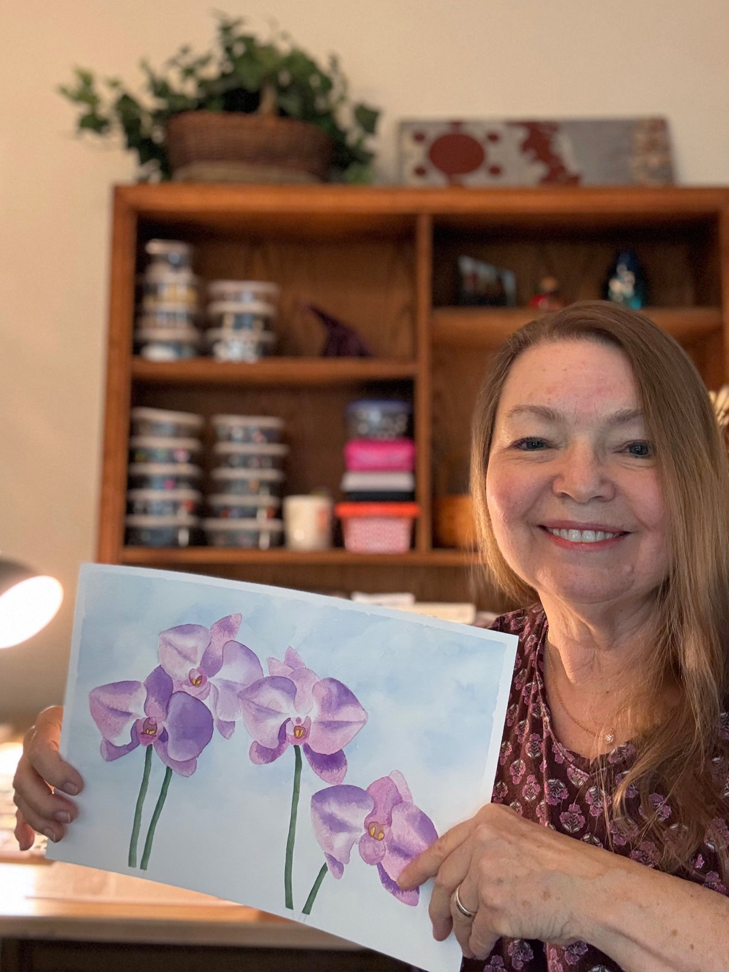 Fine artist Ruth holding her finished pink orchid watercolor painting available to acquire on Mitsooz.