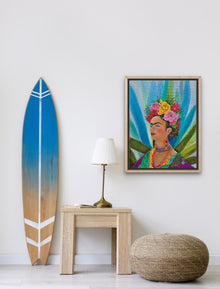 A vertical 9x12 original oil painting titled Colorful Frida by Nersel Muehlen in a light wood frame displayed in a coastal bohemian interior next to a surfboard on Mitsooz.