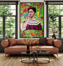A monumental 40x60 original oil painting titled Frida Kahlo by Nersel Muehlen, featuring a vibrant photorealistic portrait of the iconic artist in a Mexican dress with parrots and floral motifs. The artwork is displayed in a bright modern living room with large windows, styled above a cognac leather bolster sofa and contemporary black coffee tables on Mitsooz.