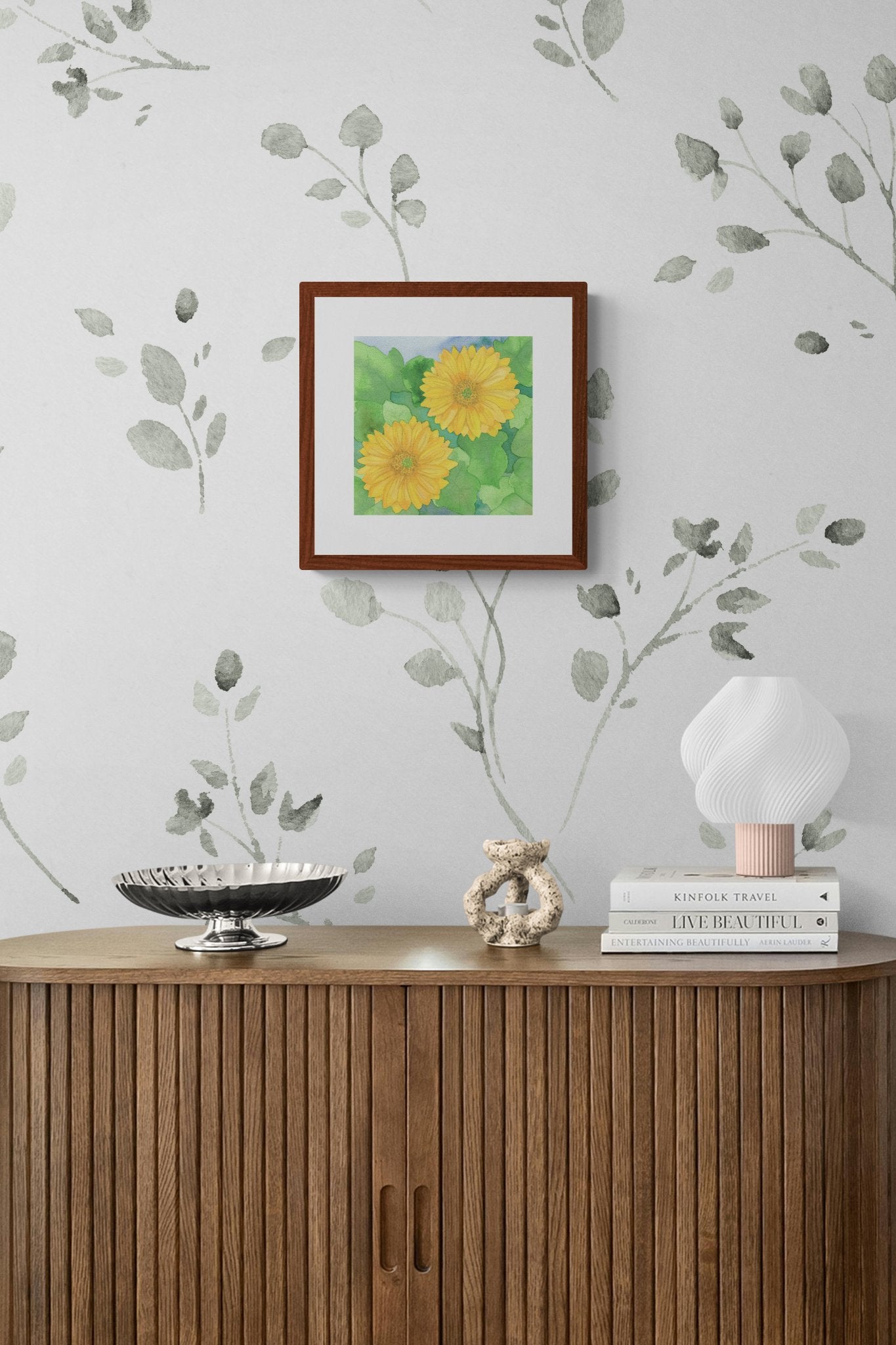 Square original watercolor titled Two Yellow Gerbera Daisies by Ruth Wall in a mahogany frame displayed in a modern interior above a wooden console on Mitsooz.
