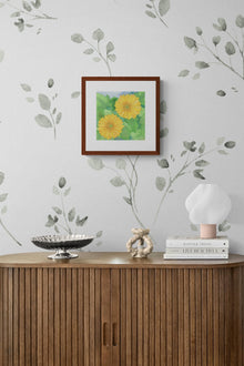 Square original watercolor titled Two Yellow Gerbera Daisies by Ruth Wall in a mahogany frame displayed in a modern interior above a wooden console on Mitsooz.