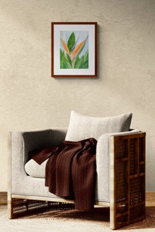 A vertical original botanical watercolor titled Words of Paradise by Ruth Wall in a mahogany frame. The artwork is hanging on a tan textured wall above a modern beige armchair styled with a dark brown textured throw on Mitsooz.