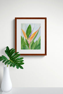 A vertical original botanical watercolor titled Words of Paradise by Ruth Wall in a mahogany frame. The artwork is hanging on a clean white wall above a minimalist white vase containing a single large green philodendron leaf on Mitsooz.