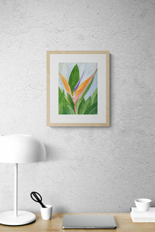 A vertical original botanical watercolor titled Words of Paradise by Ruth Wall in a natural wood frame. The artwork is styled on a white textured wall above a modern wooden desk featuring a white dome lamp and minimal office decor on Mitsooz.